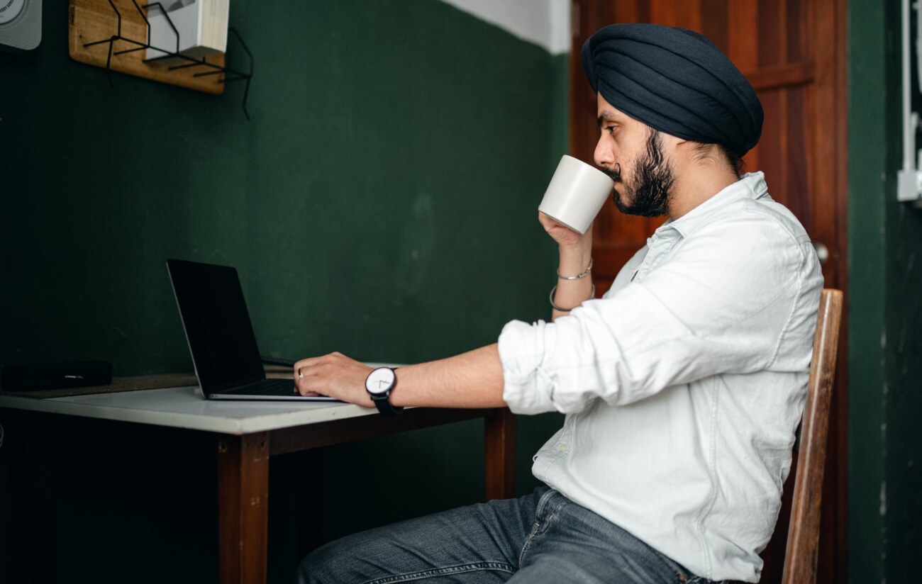 focused young indian man with cup of coffee working on netbook at home